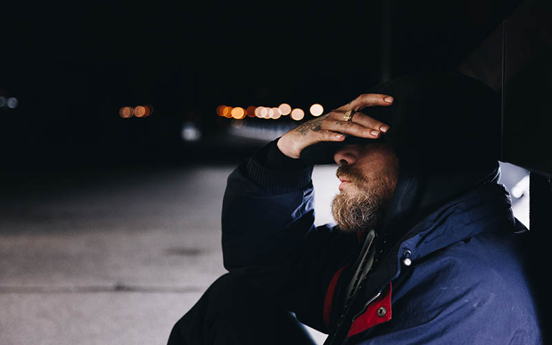 A man holding his head in his hands under a bridge