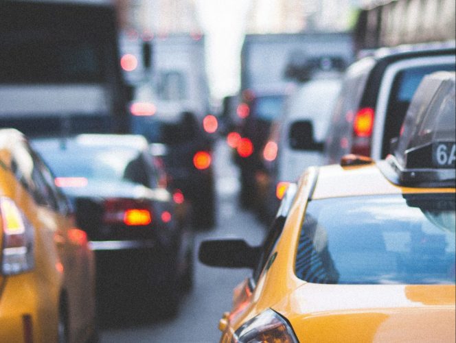 A photo of New York City traffic, viewed from the bumper of many taxis and cars waiting at an intersection