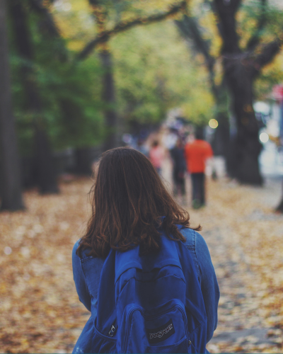 The back of a student who is walking through a park.