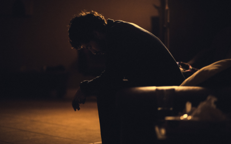 A person sadly sitting slumped over on a bench outside at night.
