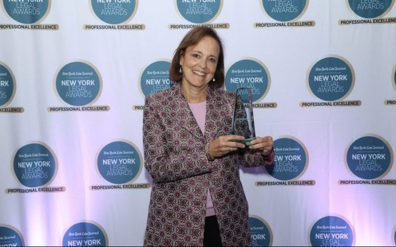 Susan Kohlmann holds up her award in front of a branded Step and Repeat for the 2022 NY Law Journal Awards.